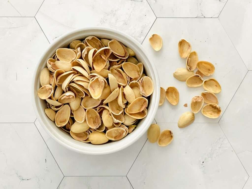 Lemon Pistachio Cake with Cream Cheese Frosting 3 Pistachio shells in a bowl with a few scattered next to it.