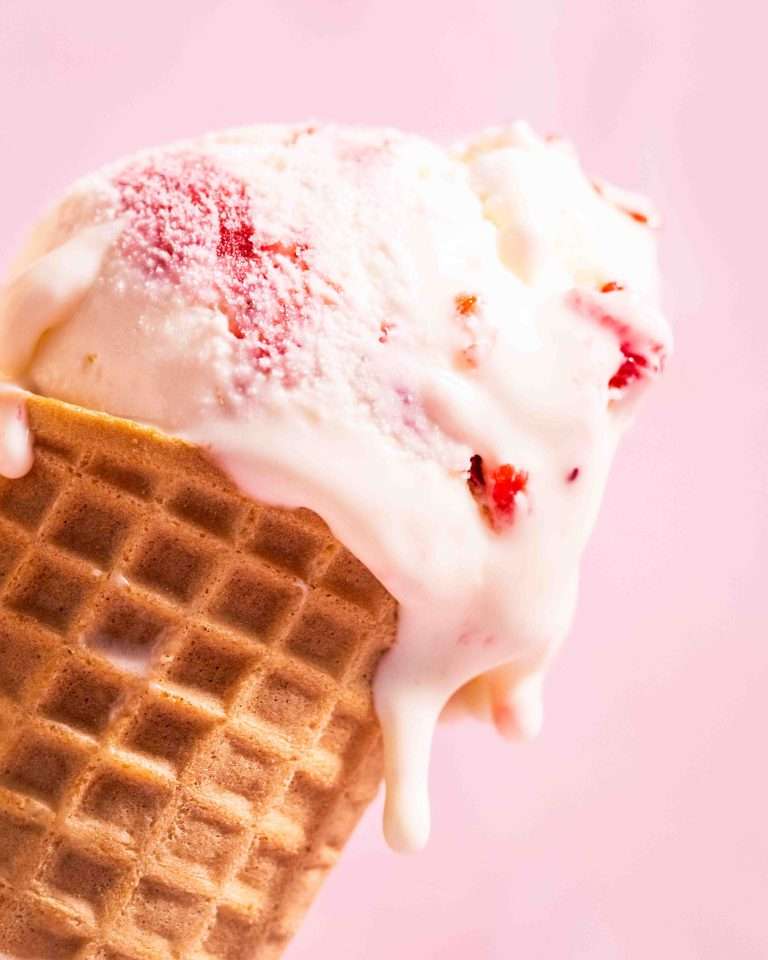 Strawberry rhubarb no churn ice cream dripping in a cone.