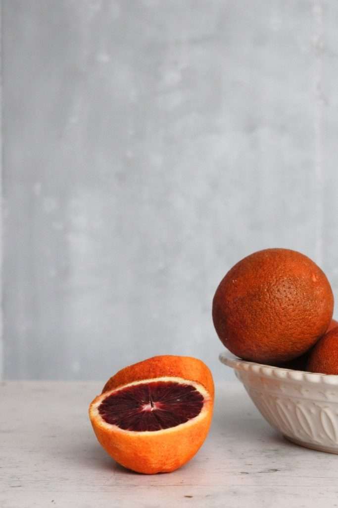 Blood Oranges in a bowl visible on the side with one cut in half.