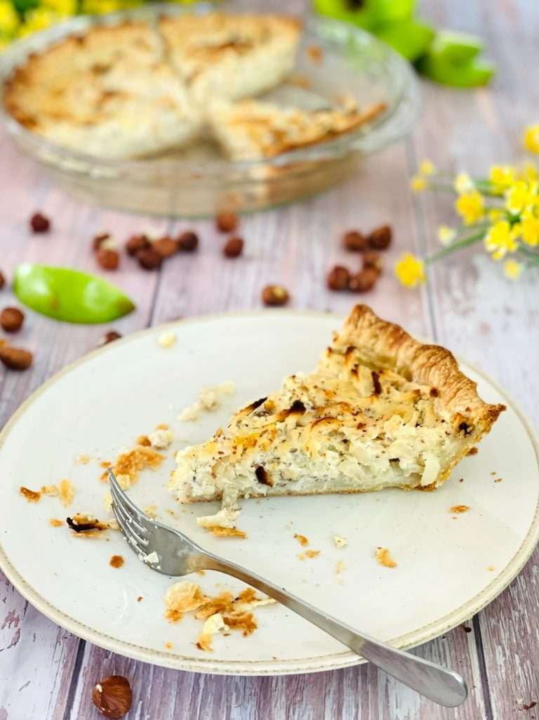 Swiss Apple Tart slice on a plate with granny smith apples seen in the background.