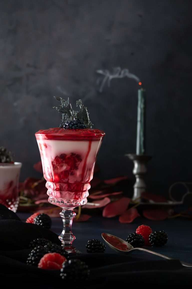 Raspberry coulis panna cotta in a glass with a blown out candle in the background.