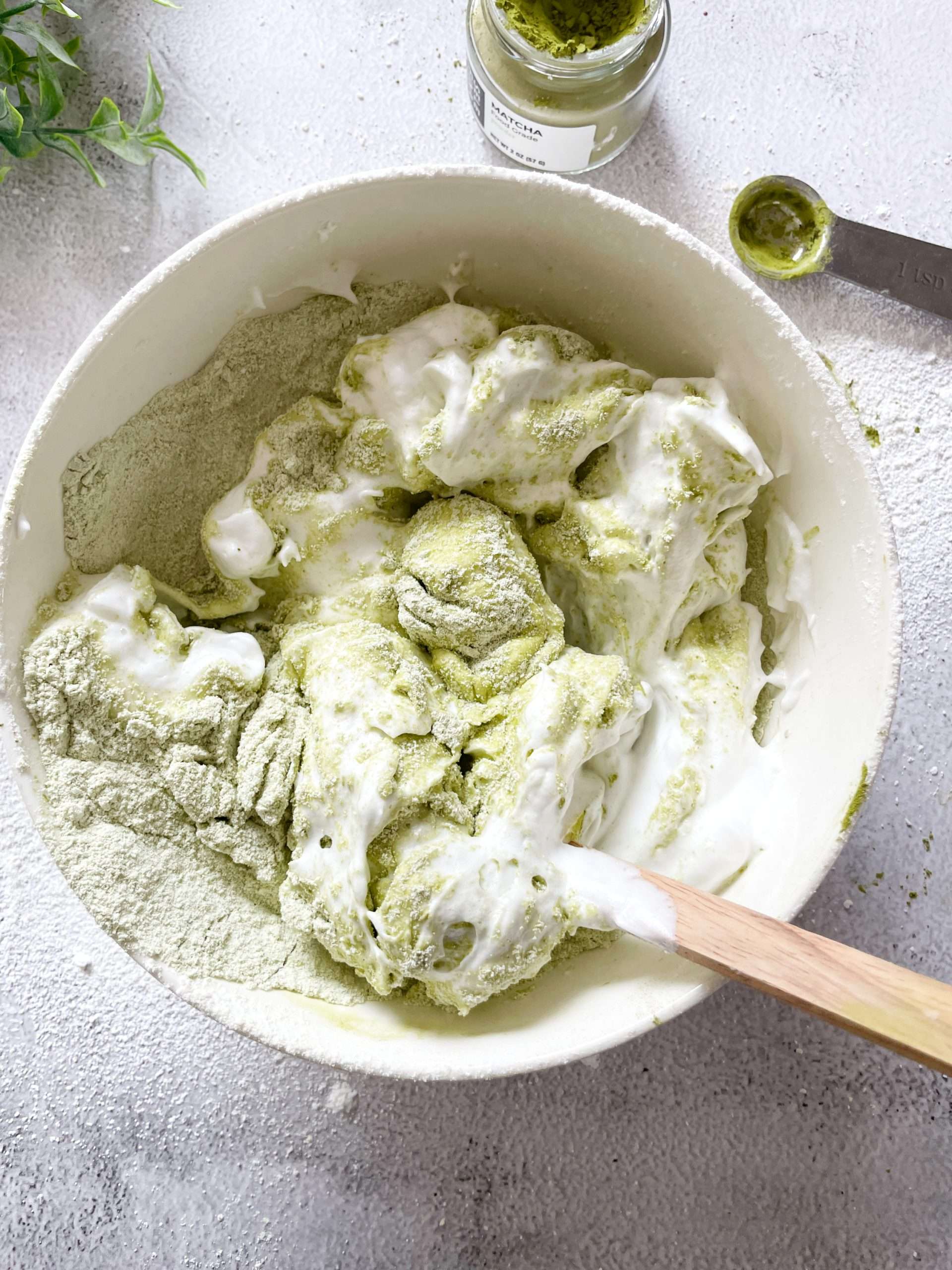 Whipped egg whites and matcha powder being mixed with a rubber spatula.