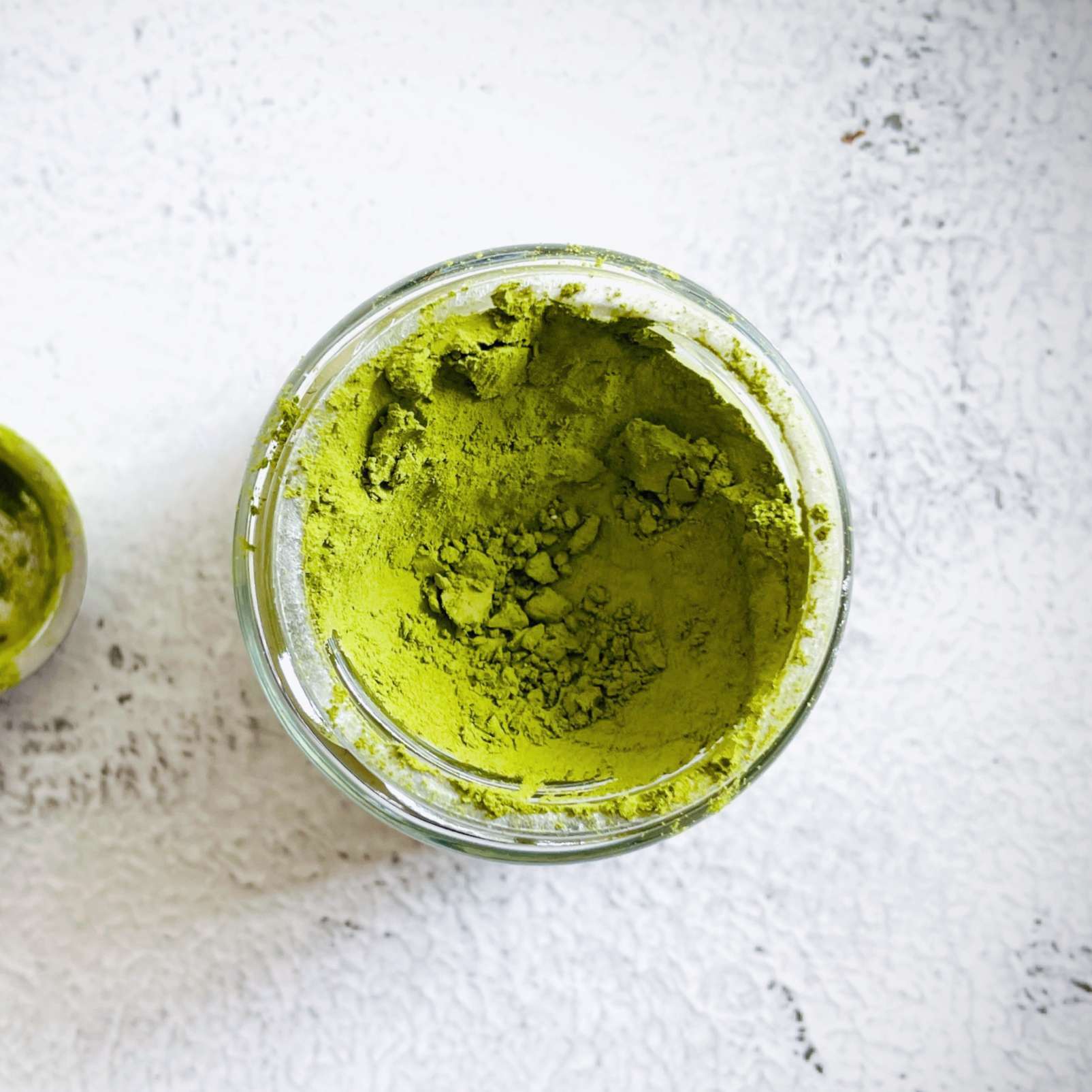 Close-up view of green matcha powder in a small glass jar.