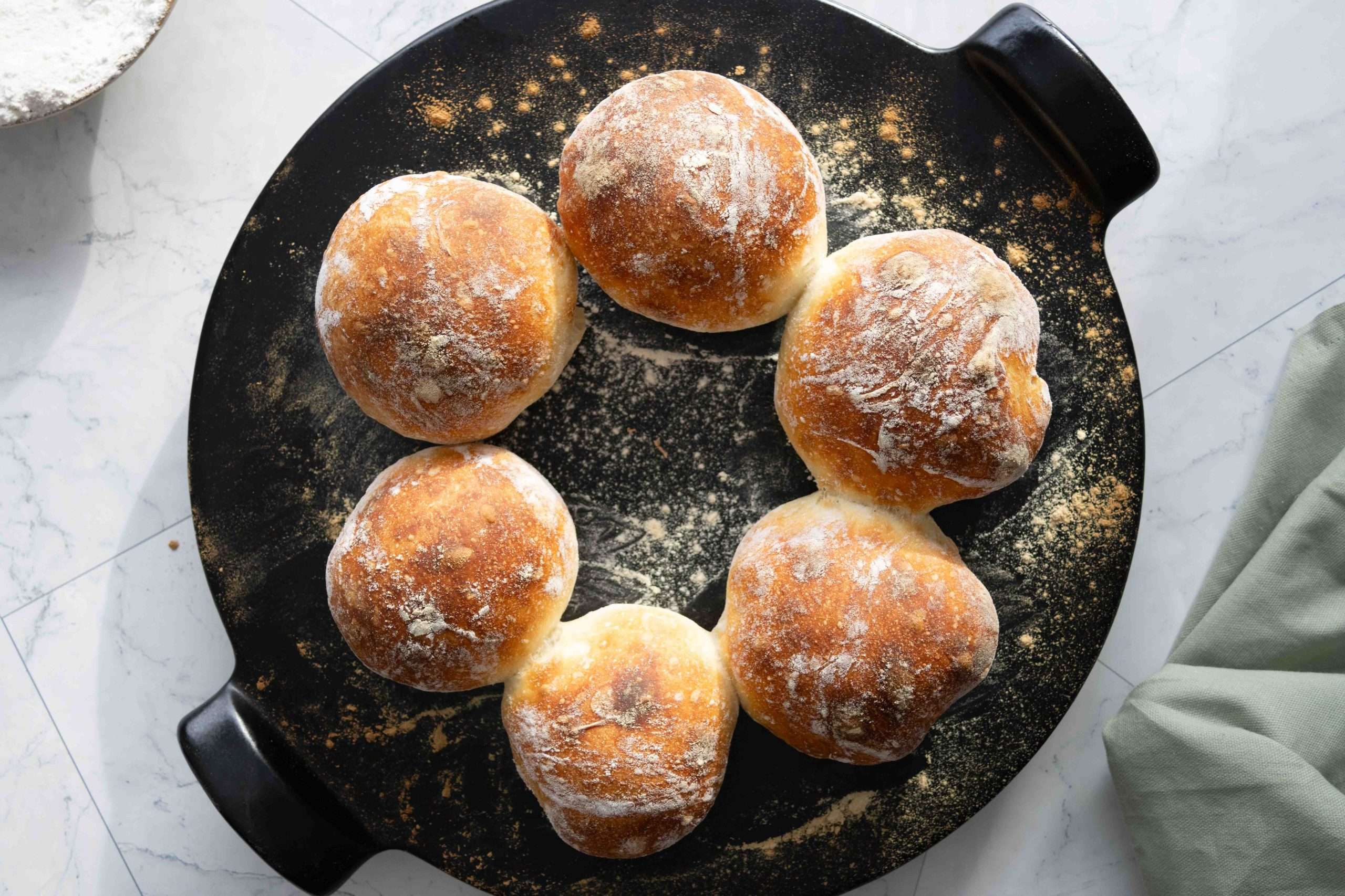 Freshly baked Swiss bread rolls called Bürli on a black pizza stone.