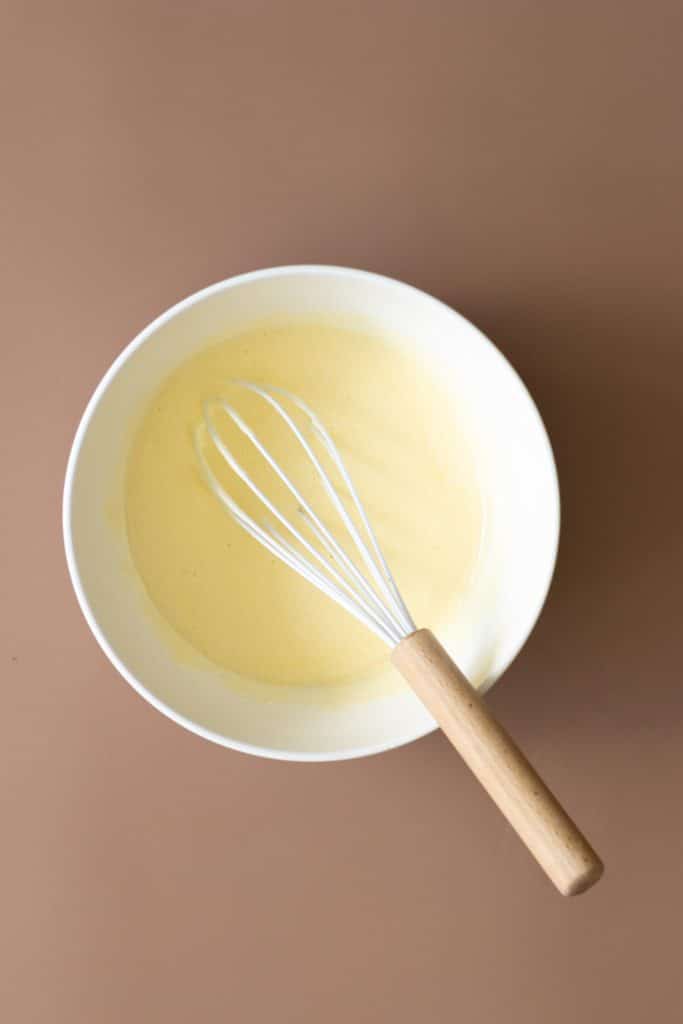 A white mixing bowl with a silky light yellow egg and sugar mixture.