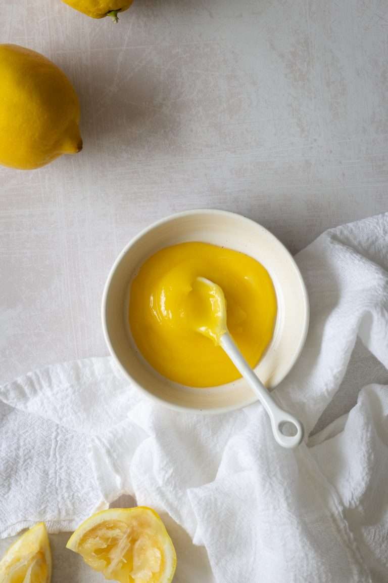 Easy lemon curd in a shallow bowl with a white ceramic spoon.