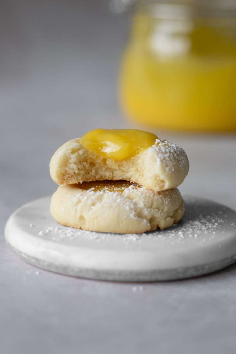A stack of two lemon curd cookies with a buttery cookie base and an indent of homemade lemon curd.