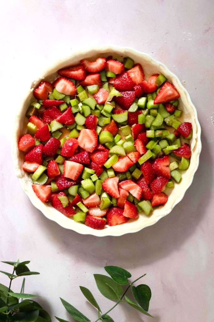 Pieces of cut strawberry and rhubarb placed into the tart shell before covering it with a latticed top.