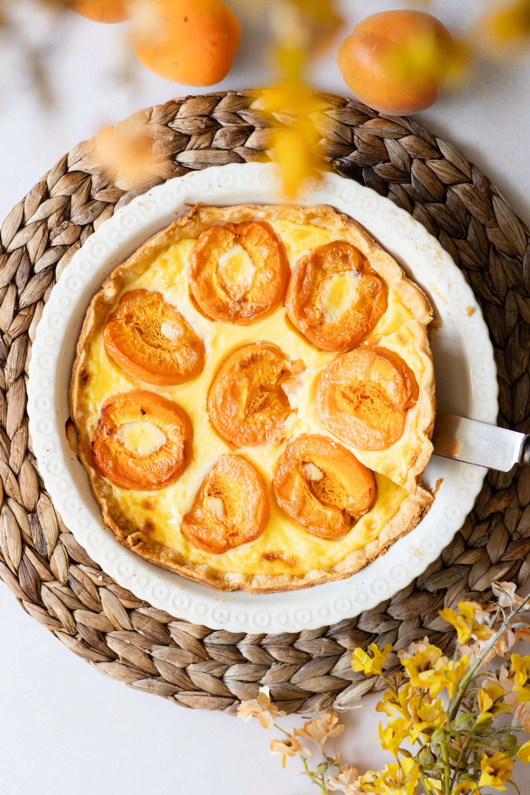 12 Easy Swiss Recipes You Can Try at Home 11 Swiss apricot tart with vanilla custard seen from the top with yellow and orange flowers seen visible on the side.
