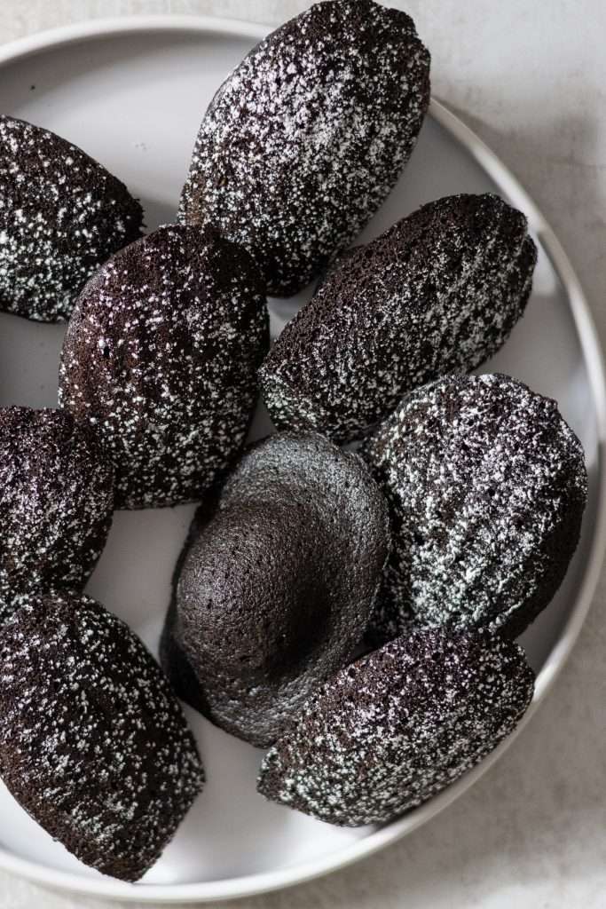 Classic Pumpkin Pie with Graham Cracker Crust 5 Chocolate madeleines dusted with powdered sugar on a round white plate.