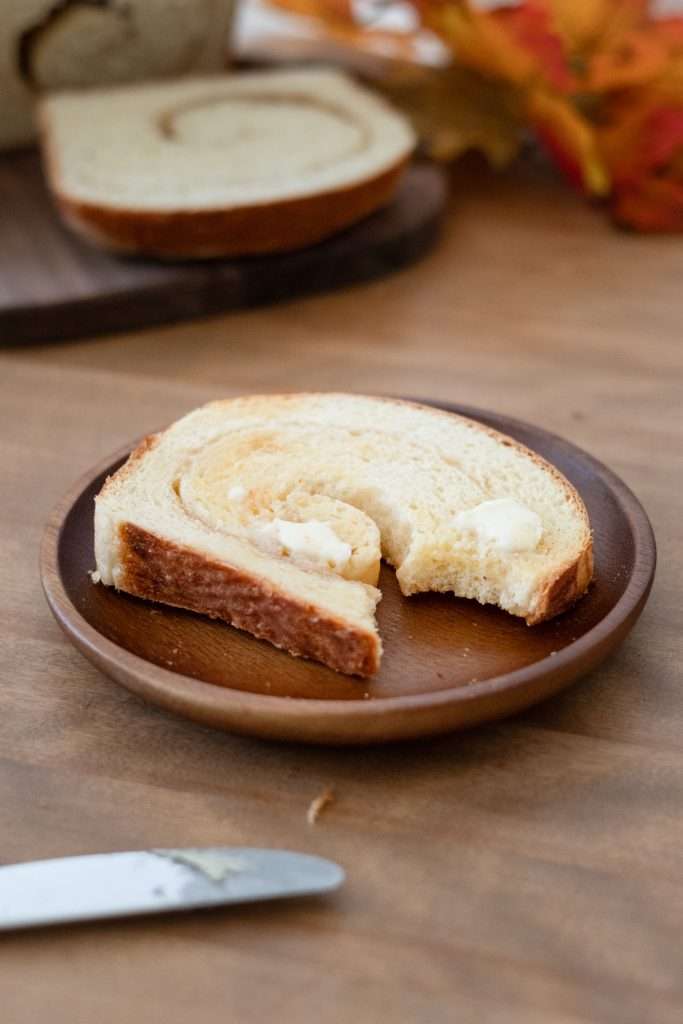 Maple Brioche with a Maple Sugar Swirl 25 Slive of maple brioche on a wooden plate with a dollop of butter half melted and a bite taken out.