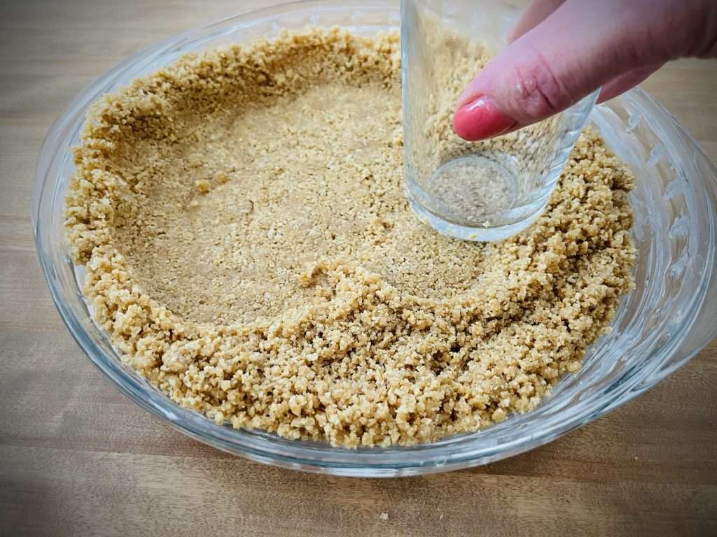Classic Pumpkin Pie with Graham Cracker Crust 9 Graham cracker crumbs being pressed into a pie dish with the bottom of a glass.